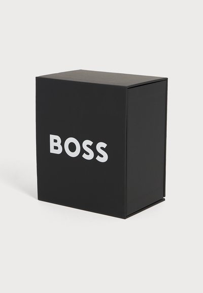 Черен правоъгълен кутия с думата BOSS с големи бели главни букви отпред, разположена на обикновен светъл фон.