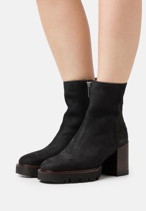 Bottes basses en daim noir avec un talon carré épais, une fermeture éclair latérale et une semelle texturée. Design simple et élégant avec des accents minimaux.
