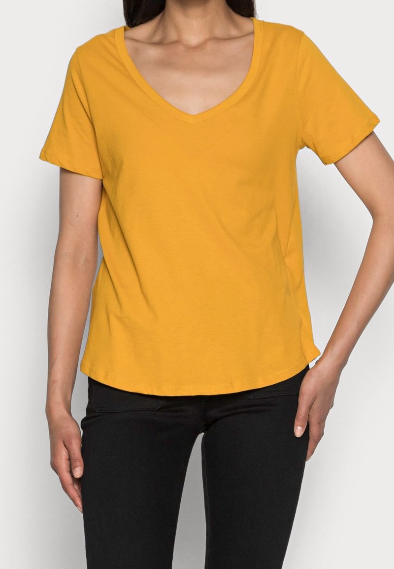 T-shirt en coton jaune à col en V avec manches courtes, coupe décontractée et ourlet arrondi, assorti à un pantalon noir. Texture lisse, sans motifs.