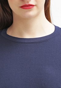 Marineblauer Strickpullover mit Rundhalsausschnitt und geripptem Design. Die Nahaufnahme hebt den glatten Stoff und die Kragendetails hervor.