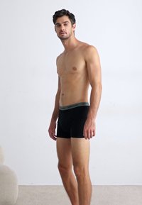 Boxer-briefs noirs avec une taille grise, offrant un ajustement serré et un tissu lisse, présentés sur un modèle devant un fond clair.