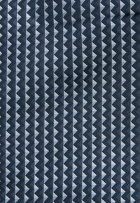 Tkanina w geometryczny wzór z zygzakowymi desenami w ciemnoniebieskich i jasnoszarych odcieniach, charakteryzująca się textured splotem oraz jednolitymi pionowymi paskami.