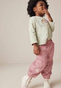 Cămașă lungă verde deschis, cu mâneci lungi și brodare "LOVE", asociată cu pantaloni cargo roz, având buzunare și manșete elastice, purtată cu adidași albi.