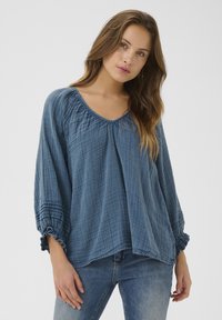 Blaue, locker sitzende Bluse aus strukturiertem Stoff mit Rundhalsausschnitt, gerafften Nähten und elastischen, gerafften Ärmeln.