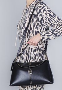 Borsa a secchiello in pelle nera con forma strutturata, hardware argentato e cuciture a contrasto. Presenta una tracolla removibile e un design elegante.