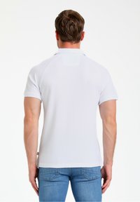 Hvid polo-shirt med et struktureret stof, korte raglanærmer og en lille krave. Båret med lyseblå denim jeans.