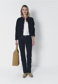 Ciemnoniebieska dżinsowa kurtka z srebrnymi guzikami, biały top, ciemne dżinsy i beżowa zamszowa torebka. Modelka nosi beżowe botki za kostkę. Prosta, casualowa stylizacja.