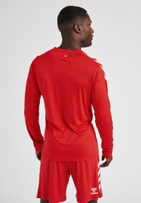 Rode sportshirts met lange mouwen, met een ronde hals en chevrons op de schouders. Gepaard met bijpassende shorts.