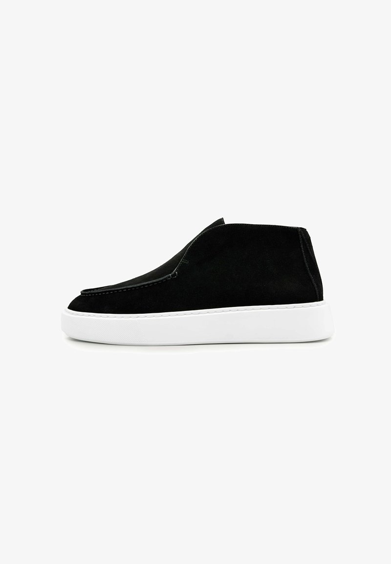 Zwarte suede instapsneaker met witte rubberen zool, minimale stiksels en lage enkelhoogte, weergegeven in zijprofiel op een witte achtergrond.