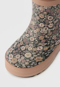 Ziedu raksts gumijas zābaks ar spīdīgu melnu fonu, kurā ir daudzkrāsaini ziedi un brūns gumijas zole un akcenti augšpusē.