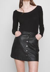 Zwart geribd topje met lange mouwen en een off-shoulder ontwerp, gecombineerd met een zwarte leren minirok met zijzakken en zilveren drukknopen.