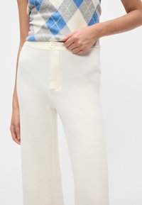 Kremasti hlače širokih nogavica iz mehkega materiala, z zapiranjem na gumb spredaj in diskretnim teksturiranim zaključkom.