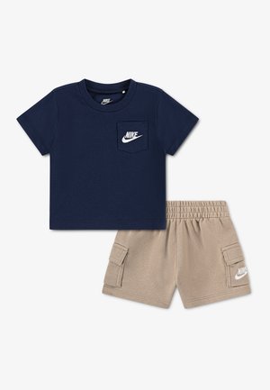 Camiseta de manga corta azul marino con logo de Nike en el bolsillo del pecho y pantalones cortos cargo beige con bolsillos laterales y logo de Nike en la pierna izquierda.