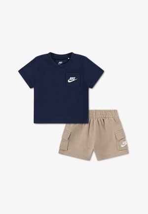 Marineblå kortærmet t-shirt med Nike-logo på brystlommen og beige cargobukser med sidelommer og Nike-logo på venstre ben.