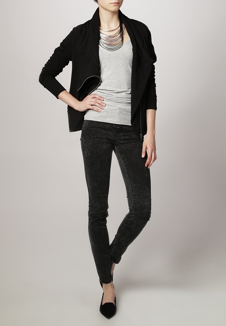 Svart draperad jacka över en grå tanktop, ihop med mörkgrå skinny jeans och svarta spetsiga ballerinaskor. Har ett lagrat silverhalsband.