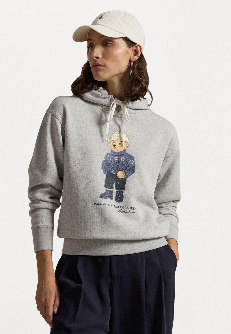 Siv sweatshirts iz bombažom z barvitim grafičnim prikazom polo medveda, oblečenega v vzorčasto jopico. Vključuje kapuco z vrvico in rebrastim zaključkom na rokavih.
