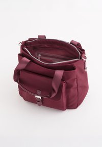 Bordeaux stof håndtaske med dobbelte håndtag, lynlåslåg og frontlomme med klap. Har sølvfarvet hardware og en glat overflade.
