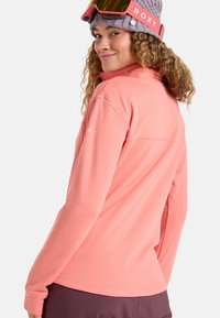 Light pink long-sleeve fleece with a textured pattern, features a half-zip collar, Roxy logo on the sleeve, and contrasting dark pants.