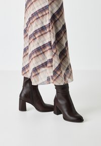 Brown leather ankle boots with a square toe, chunky heel, and visible side zipper. The design features a smooth texture and fitted shaft.
