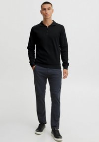 Black long-sleeve pullover with a zippered collar, paired with dark blue pants and black sneakers. Features a fitted design and ribbed cuffs.