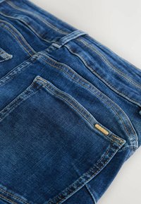 Mėlynos džinsinės kelnės su klasikinio kirpimo, su siuvinėjimo detalėmis ir maža auksine etikete, pažymėta "NEXT". Galinis kišenė su lygia tekstūra.