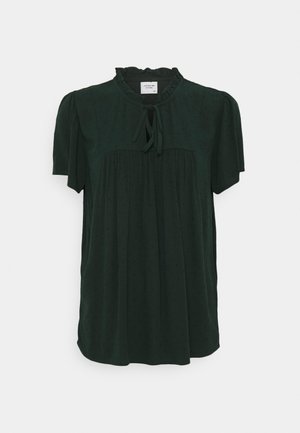 Blusa verde a maniche corte realizzata in un tessuto morbido. Presenta un collo arricciato e un dettaglio con cravatta nella parte anteriore. Motivo texture sottile in tutta la superficie.