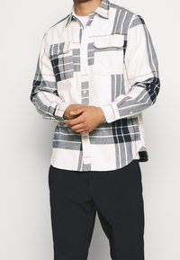 Camicia in flanella con base bianca e fantasia a quadri navy, grigia e rosa chiaro, colletto button-down e due tasche sul petto.
