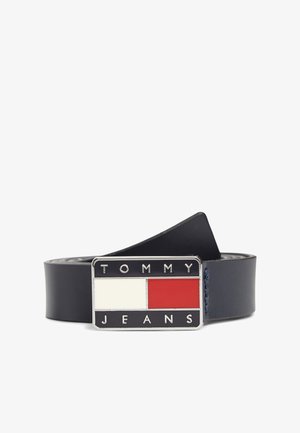 Usnjen pas v mornarsko modri barvi z pravokotno zaponko, ki ima rdeče in bele dele, z vtisnjenim napisom "TOMMY JEANS" v srebrni barvi.