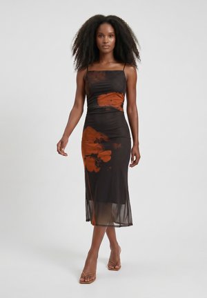 Woman with natural curly hair walking, wearing a fitted black midi dress with large orange floral prints and tan heeled sandals.