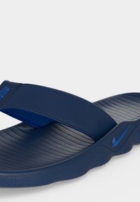 Σανδάλι slide της Nike σε ναυτικό μπλε χρώμα με υφή στην πατούσα, φαρδιά λουρίδα και μικρό λογότυπο swoosh στη πλευρά κοντά στη σόλα.