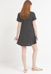 Vestido corto negro con patrón floral, dobladillo acampanado y textura ligera. Combinado con bailarinas metálicas y puntiagudas.