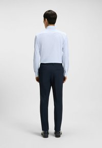 Vaaleansinisessä kuosisessa pitkähihaisessa paidassa on nappikaulus ja nappimansetit, pehmeä kangas ja hyvin istuva leikkaus. Paita on yhdistetty tummansiinisiin housuihin.