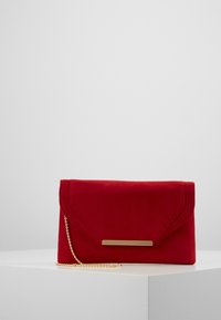 Pochette en daim rouge avec un accent en métal doré et une bandoulière chaîne. Présente un rabat à angle et une texture lisse.