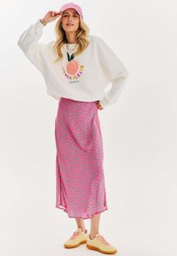 Bílá mikina s grafikou "PEACH PLEASE", růžová midi sukně s puntíky a žluté tenisky. Lehký materiál s volným střihem.