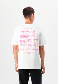 Hvit bomulls t-skjorte med rosa grafiske trykk på ryggen, inkludert logoer og tekst, med korte ermer og en avslappet passform.
