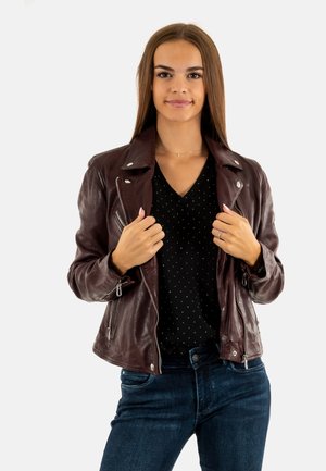 Giubbotto di pelle bordeaux con zip asimmetrica, polsini con zip e colletto classico, abbinato a un top nero a pois e jeans scuri.
