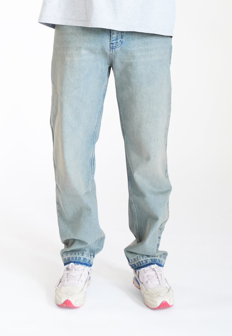 Jeans de mezclilla azul claro con un corte relajado, que cuentan con bolsillos laterales y detalles de costura, combinados con zapatillas blancas con acentos rosas.