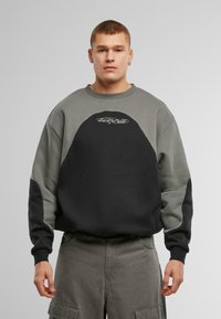 Sudadera con bloques de color en gris y negro. Cuenta con un escote redondo, mangas raglán y detalle de logo en el pecho. Textura suave.