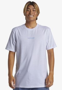 Camiseta de algodón blanca de manga corta, con un logo azul de "Quiksilver" en el centro. Diseño simple de cuello redondo, textura suave.