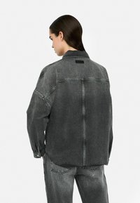 Graues Denim-Hemd mit lockerer Passform, langen Ärmeln und Druckknöpfen. Verfügt über eine Rückenpasse und ein kleines Logo-Patch. Strukturiertes Material.