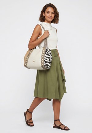 Woman wearing white sleeveless top and olive green skirt, carrying large beige handbag with zebra print and pearl details over shoulder.