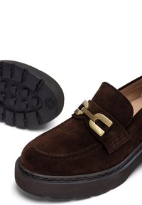 Mocassino in suede marrone con dettaglio di fibbia in tono dorato, caratterizzato da una suola in gomma nera spessa con un motivo testurizzato per la presa.