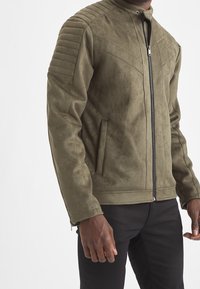 Olive green suede jacket with ribbed shoulder detailing, front zip closure, and side pockets. Smooth texture and fitted design.