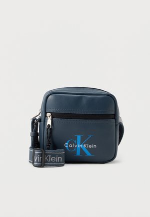 Petit sac bandoulière bleu marine avec poche avant zippée, sangle réglable et logo Calvin Klein en bleu et blanc sur le panneau avant.