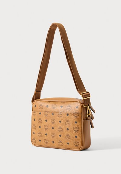 Τσαντάκι crossbody από ταμπά δέρμα με ρυθμιζόμενο καφέ υφασμάτινο ιμάντα, χρυσά μεταλλικά στοιχεία και επαναλαμβανόμενο μοτίβο λογότυπου MCM σε υφή επιφάνειας.