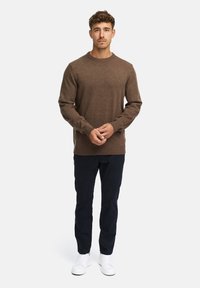 Brązowy sweter dziany z okrągłym dekoltem, w zestawie z granatowymi spodniami i białymi trampkami. Prosty design, gładka tekstura i brak widocznych wzorów.