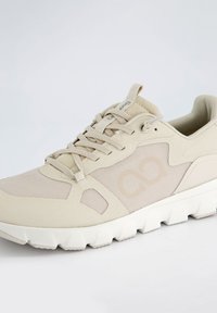 Chaussure de sport beige avec des panneaux en mesh, du daim texturé et une semelle en caoutchouc blanc avec un motif de semelle hexagonale.