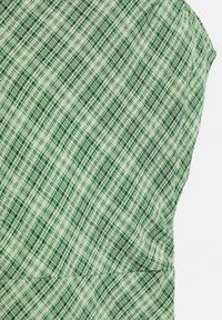 Tissu à carreaux vert et blanc avec des lignes diagonales et horizontales formant un motif quadrillé, montrant la texture et les détails de couture.