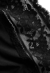 Tessuto di pizzo nero con motivi floreali, caratterizzato da dettagli intricati e bordi scallopati, a contrasto con uno sfondo nero liscio.