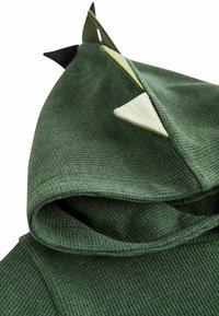 Gros plan sur une capuche en tissu tricoté gaufré vert avec trois pointes en tissu de différentes nuances de vert le long de la couture supérieure.